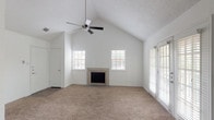 This single-story, one-bedroom, one-bathroom home is thoughtfully designed to maximize comfort and functionality. The living room serves as the centerpiece of the space, featuring dramatic vaulted ceilings that amplify the sense of openness, a ceiling fan, soft wall-to-wall carpeting, and a tile-surround fireplace that adds warmth and character. Multiple windows with slatted blinds and a set of French doors flood the room with natural light while providing access to the outdoors.

The kitchen is well-appointed with an abundance of raised-panel gray cabinetry offering plentiful storage, light-toned countertops, a stainless steel sink, and white appliances including a range and refrigerator. Dark wood-style flooring grounds the space, and a peninsula counter with a breakfast bar creates a seamless connection to the adjacent dining and living areas. Pendant lighting above the peninsula adds a stylish finishing touch. A built-in shelving unit is conveniently integrated near the transition between the kitchen and living spaces, offering additional display and storage options.

The bedroom continues the vaulted ceiling design, featuring carpet flooring, a ceiling fan, and dual windows that invite natural light. The clean, neutral palette throughout the entire home creates a bright, versatile backdrop ready for personalization.