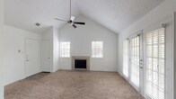 This single-story, one-bedroom, one-bathroom home is thoughtfully designed to maximize comfort and functionality. The living room serves as the centerpiece of the space, featuring dramatic vaulted ceilings that amplify the sense of openness, a ceiling fan, soft wall-to-wall carpeting, and a tile-surround fireplace that adds warmth and character. Multiple windows with slatted blinds and a set of French doors flood the room with natural light while providing access to the outdoors.

The kitchen is well-appointed with an abundance of raised-panel gray cabinetry offering plentiful storage, light-toned countertops, a stainless steel sink, and white appliances including a range and refrigerator. Dark wood-style flooring grounds the space, and a peninsula counter with a breakfast bar creates a seamless connection to the adjacent dining and living areas. Pendant lighting above the peninsula adds a stylish finishing touch. A built-in shelving unit is conveniently integrated near the transition between the kitchen and living spaces, offering additional display and storage options.

The bedroom continues the vaulted ceiling design, featuring carpet flooring, a ceiling fan, and dual windows that invite natural light. The clean, neutral palette throughout the entire home creates a bright, versatile backdrop ready for personalization.