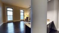 This single-floor residence showcases a thoughtfully designed open layout that seamlessly connects the kitchen and living areas. Dark hardwood floors run throughout, providing a rich, warm contrast to the neutral, light-toned walls. A marble-topped kitchen counter serves as a functional divider between the kitchen and the main living space, offering both workspace and a visual anchor for the layout.

The living area is centered around an elegant arched window, a standout architectural detail that allows natural light to filter in and lends a classic character to the space. The window's arched design adds a refined aesthetic touch, complementing the clean lines of the surrounding walls and white baseboards. A wall-mounted projector is also present, adding a modern amenity to the space.

Crown molding along the ceiling further enhances the traditional elegance of the unit. The overall ambiance is warm and intimate, enhanced by soft floor lamp lighting positioned near a classic wingback armchair, creating a cozy reading nook by the window. The space balances timeless architectural details with practical, comfortable living features.