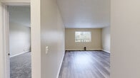 This single-floor unit offers a clean, functional layout with a neutral color palette throughout, creating a bright and inviting atmosphere. The living area is a standout feature, showcasing modern grey laminate flooring that reflects natural light from a large window overlooking greenery outside. The open feel of the space makes it highly versatile for various furniture arrangements.

The bedrooms are carpeted for comfort and feature textured ceilings consistent with the rest of the unit. At least one bedroom includes a built-in closet with classic louvered bi-fold doors, providing ample storage. A window in one of the bedrooms allows natural light to filter in, offering pleasant outdoor views.

The kitchen is equipped with white cabinetry, laminate countertops, a stainless steel sink with a modern faucet, and a white dishwasher, providing a practical and tidy workspace. The flooring continues the laminate theme seen in the main living area.

The bathroom is well-appointed with a single-sink vanity featuring white cabinetry, a large mirror, tile-accented walls, and a tub-shower combination with a patterned curtain. The wood-look flooring adds a contemporary touch to this functional space.

Overall, the unit presents a cohesive, move-in-ready interior with consistent finishes and ample natural light throughout.