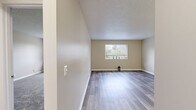 This single-floor unit offers a clean, functional layout with a neutral color palette throughout, creating a bright and inviting atmosphere. The living area is a standout feature, showcasing modern grey laminate flooring that reflects natural light from a large window overlooking greenery outside. The open feel of the space makes it highly versatile for various furniture arrangements.

The bedrooms are carpeted for comfort and feature textured ceilings consistent with the rest of the unit. At least one bedroom includes a built-in closet with classic louvered bi-fold doors, providing ample storage. A window in one of the bedrooms allows natural light to filter in, offering pleasant outdoor views.

The kitchen is equipped with white cabinetry, laminate countertops, a stainless steel sink with a modern faucet, and a white dishwasher, providing a practical and tidy workspace. The flooring continues the laminate theme seen in the main living area.

The bathroom is well-appointed with a single-sink vanity featuring white cabinetry, a large mirror, tile-accented walls, and a tub-shower combination with a patterned curtain. The wood-look flooring adds a contemporary touch to this functional space.

Overall, the unit presents a cohesive, move-in-ready interior with consistent finishes and ample natural light throughout.