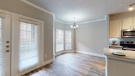 This single-floor residence combines classic architectural details with modern finishes to create a comfortable and stylish living environment. Throughout the space, warm hardwood-style flooring and crisp crown molding provide a cohesive, polished look, while neutral gray walls offer a versatile backdrop.

The dining area features a graceful bay window configuration that floods the room with natural light, complemented by an elegant chandelier overhead. Adjacent to it, the living area is equally bright, with French doors opening to the outdoors and a ceiling fan for added comfort. Both spaces benefit from generous proportions and a seamless flow between them.

The kitchen is well-equipped with stainless steel appliances, white cabinetry, a decorative tile backsplash, track lighting, and a granite-topped peninsula with an undermount sink — ideal for both everyday use and entertaining.

The bedrooms are comfortably sized, each featuring ceiling fans, hardwood-style floors, and ample natural light through window blinds. Crown molding carries through these rooms, maintaining the home's refined aesthetic.

The bathroom offers a clean, contemporary design with a granite vanity, gray cabinetry with brushed gold hardware, large-format tile surrounding the tub-shower combo, and wood-look flooring. A dedicated in-unit laundry area with overhead shelving adds everyday convenience to this well-rounded residence.