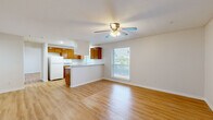 This single-story, one-bedroom, one-bathroom residence in Austin, TX is thoughtfully organized to maximize its compact footprint. Warm-toned hardwood-style flooring runs consistently throughout the entire unit, creating a cohesive and inviting atmosphere.

The open-concept living and kitchen area forms the heart of the unit. The kitchen features warm wood cabinetry, a peninsula breakfast bar with a cooktop, a ceiling-mounted range hood, a white refrigerator, and a sink positioned beneath a window that brings in natural light. The adjacent living area is bright and airy, enhanced by a ceiling fan with integrated lighting and a window overlooking an outdoor balcony railing with greenery beyond.

The bedroom is a well-proportioned private retreat, also equipped with a ceiling fan and a window with outdoor views. It includes access to a dedicated walk-in closet outfitted with dual hanging rods on both sides and a central built-in shelving unit, providing generous and organized storage.

The bathroom is cleanly finished, featuring a wood-toned vanity with a light stone-style countertop, a large mirror, and a full tub-shower combination enclosed in white tile. White walls and neutral tones throughout the unit contribute to a clean, functional, and consistent aesthetic.