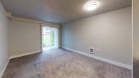 Located at 25920 112th Ave SE in Kent, Washington, this single-floor unit offers a functional and straightforward layout designed for comfortable everyday living. The living area is generously proportioned, finished with plush carpet underfoot and neutral-toned walls that create a calm, understated atmosphere. A prominent sliding glass door fitted with vertical blinds serves as the focal point of the living space, allowing natural light to filter in while providing direct views of a green outdoor area. The textured ceiling adds a classic touch consistent throughout the main living spaces.

A hallway connects the living area to the rest of the unit, where a closet with sliding doors provides convenient storage. The kitchen is equipped with modern stainless steel appliances, including a range, over-the-range microwave, and a full-size refrigerator, complemented by light wood-look flooring and white cabinetry with clean countertops. The bedroom features carpeted flooring, a window with blinds overlooking a green space, and a baseboard heater. The bathroom is finished with warm wood-look flooring, a vanity with dark cabinetry, and a bathtub, offering a clean and practical design throughout.