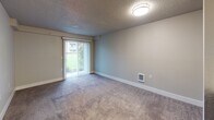Located at 25920 112th Ave SE in Kent, Washington, this single-floor unit offers a functional and straightforward layout designed for comfortable everyday living. The living area is generously proportioned, finished with plush carpet underfoot and neutral-toned walls that create a calm, understated atmosphere. A prominent sliding glass door fitted with vertical blinds serves as the focal point of the living space, allowing natural light to filter in while providing direct views of a green outdoor area. The textured ceiling adds a classic touch consistent throughout the main living spaces.

A hallway connects the living area to the rest of the unit, where a closet with sliding doors provides convenient storage. The kitchen is equipped with modern stainless steel appliances, including a range, over-the-range microwave, and a full-size refrigerator, complemented by light wood-look flooring and white cabinetry with clean countertops. The bedroom features carpeted flooring, a window with blinds overlooking a green space, and a baseboard heater. The bathroom is finished with warm wood-look flooring, a vanity with dark cabinetry, and a bathtub, offering a clean and practical design throughout.