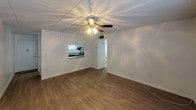 This single-story space offers a straightforward, functional layout across several distinct areas. The living room is finished with wood-look vinyl flooring and features a ceiling fan with integrated lighting and a textured ceiling. A pass-through window connects the living area directly to the kitchen, creating an open feel between the two spaces. The kitchen is equipped with dark wood cabinetry, a coil-top electric range with an overhead ventilation hood, a single-basin stainless steel sink, and laminate countertops, with a window providing natural light.

The bedrooms are carpeted and feature textured ceilings. One bedroom includes a ceiling fan with lighting, while both bedrooms are notably equipped with dual sliding closets, offering generous built-in storage with hanging rods. Natural light enters through blinds-covered windows. An additional carpeted room provides flexible space without a ceiling fan.

The bathroom features wood-look vinyl flooring, a vanity with a stone-look countertop and wood cabinetry, a toilet, and a full tub-shower combination with a window above. White walls throughout the unit maintain a clean, neutral aesthetic, creating a bright and practical living environment.