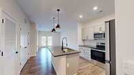Located in Huntersville, NC, this well-appointed single-story home offers four bedrooms, two bathrooms, and a thoughtfully designed layout that maximizes functionality. The open-concept kitchen serves as the heart of the home, showcasing white shaker-style cabinetry with dark hardware, dark granite countertops, a subway tile backsplash, and a full suite of stainless steel appliances including a refrigerator, range, and microwave. A central island with a deep sink and sleek matte black faucet provides additional prep space and flows seamlessly into the living area, which features French doors that invite natural light and outdoor access. Hardwood-style flooring runs throughout the home, lending warmth and cohesion to every room. The primary bedroom is generously sized, boasting vaulted ceilings, a ceiling fan, and direct access to a walk-in closet with wire shelving. The en-suite bathroom features dark granite countertops, white cabinetry, and a glass-enclosed walk-in shower with matte black fixtures. Additional bedrooms are bright and comfortable, each with ceiling fans and natural light from sizable windows. A second full bathroom offers a vanity with matching finishes and a natural light window. Three closets provide ample storage throughout the home.
