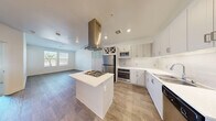 Located in Henderson, NV, this 1-bedroom, 1-bathroom residence offers a thoughtfully designed open-concept layout that seamlessly connects the living, dining, and kitchen areas. The kitchen is a standout feature, showcasing white shaker cabinetry, white quartz countertops, a subway tile backsplash, and a full suite of stainless steel appliances including a gas cooktop, wall oven, built-in microwave, refrigerator, and dishwasher. A central island with an overhead statement range hood serves as the kitchen's focal point, while a built-in wine rack adds a stylish touch. Wood-look flooring flows throughout the main living areas, complemented by recessed lighting that keeps the space bright and airy. The living area benefits from natural light through a window overlooking a landscaped exterior. The bedroom features plush carpeting, a sliding glass door opening to a private balcony with open views, and access to a dedicated closet. The clean, all-white bathroom includes a soaking tub, shower, single vanity, and wood-look tile flooring. Additional conveniences include an in-unit laundry area and a utility room, rounding out this efficiently designed home.