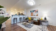 This two-floor residence offers a well-designed layout that balances functionality with a contemporary aesthetic. The main level centers around an open-concept living and dining area, where rich hardwood-style flooring, a plush area rug, and modern furnishings create a welcoming atmosphere. A breakfast bar with metal stools connects the living space to the kitchen, which is equipped with stainless steel appliances — including a full-size refrigerator, electric range, microwave, and dishwasher — paired with crisp white cabinetry and light countertops. In-unit washer and dryer connections are conveniently located adjacent to the kitchen. A staircase with a white metal railing leads to the upper level, where carpeted bedrooms provide a quieter retreat. Each bedroom features built-in closet storage, and one room includes mirrored sliding closet doors with shelving. Windows in the bedrooms allow for natural light. Multiple bathrooms are distributed across both floors, finished with hardwood-style flooring and clean, neutral fixtures. The overall design is bright and cohesive, with white walls and consistent flooring choices that unify the space across both levels.
