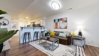 This two-floor residence offers a well-designed layout that balances functionality with a contemporary aesthetic. The main level centers around an open-concept living and dining area, where rich hardwood-style flooring, a plush area rug, and modern furnishings create a welcoming atmosphere. A breakfast bar with metal stools connects the living space to the kitchen, which is equipped with stainless steel appliances — including a full-size refrigerator, electric range, microwave, and dishwasher — paired with crisp white cabinetry and light countertops. In-unit washer and dryer connections are conveniently located adjacent to the kitchen. A staircase with a white metal railing leads to the upper level, where carpeted bedrooms provide a quieter retreat. Each bedroom features built-in closet storage, and one room includes mirrored sliding closet doors with shelving. Windows in the bedrooms allow for natural light. Multiple bathrooms are distributed across both floors, finished with hardwood-style flooring and clean, neutral fixtures. The overall design is bright and cohesive, with white walls and consistent flooring choices that unify the space across both levels.