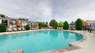 Located at 221 Plus Park Blvd in Nashville, Tennessee, this two-floor property features a well-appointed outdoor community area centered around a generously sized swimming pool. The pool itself is designed with a curved, freeform shape and offers clearly marked depth indicators, ensuring safety for all users. The surrounding pool deck is finished in a smooth concrete surface, providing ample space for lounging chairs, shaded umbrella seating, and outdoor furniture arrangements.

Adjacent to the pool is a charming clubhouse structure clad in gray shingle siding with brick accents, large windows, and a gabled roofline. This building serves as a functional hub for the community and is accessible through a decorative wrought iron gate. The surrounding landscape is thoughtfully maintained, featuring neatly trimmed topiary shrubs, flowering crape myrtle trees, and lush greenery that create a sense of privacy and a welcoming outdoor atmosphere.

A dedicated patio lounge area with teak wood furniture and teal cushioned seating is nestled among the landscaping, offering a relaxed space to unwind. The multi-story residential buildings visible in the background complement the community's cohesive architectural style. Overall, this outdoor amenity area presents a vibrant, resort-like environment ideal for recreation and community gathering.