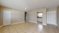 Located at 1705 17th Ave N in Saint Petersburg, Florida, this single-story home offers a straightforward and functional layout finished consistently with light beige ceramic tile flooring throughout every room. The interior is painted in warm neutral tones, contributing to a bright and cohesive atmosphere across the living spaces.

The main living area is generously proportioned, featuring large windows fitted with horizontal blinds that allow ample natural light to fill the space. A textured ceiling adds subtle visual detail overhead, while clean white baseboards frame the floors throughout. The open layout connects the living area to additional rooms with ease, creating a practical flow through the home.

The kitchen is efficiently arranged with white cabinetry, dark countertops, a double-basin sink positioned beneath a window, and white appliances including a refrigerator, electric range, and over-the-range microwave. Adjacent rooms serve as bedrooms, each benefiting from one or more windows that bring in natural light and provide ventilation.

The bathroom is cleanly appointed with a white vanity, a wall-mounted light fixture, a window for natural light, and a full tub-shower combination. Throughout the home, the consistent use of tile flooring, neutral walls, and white trim creates a unified, easy-to-maintain interior.