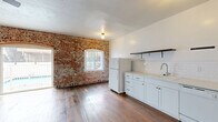 Located in the heart of Hollywood, this studio combines vintage character with modern updates across a single, well-utilized floor. The open-plan kitchen and living area is the centerpiece of the space, anchored by a striking exposed brick wall featuring a dramatic arched window that frames views of an outdoor pool. Rich, dark hardwood floors run throughout, adding warmth and continuity to the layout. A ceiling fan overhead provides comfort and enhances the airy feel of the living area. The kitchen is thoughtfully appointed with white shaker cabinetry, a subway tile backsplash, open floating shelves, a gas range with a stainless steel hood, a dishwasher, and a full-size refrigerator. A steel entry door and a wall-mounted electrical panel add an industrial edge to the space. The bathroom showcases classic finishes, including white subway tile surrounding a soaking tub with shower, a pedestal sink, and a charming black-and-white floral hexagon tile floor, all brightened by a window. The unit also includes a wall-mounted mini-split air conditioning system for year-round climate control. This studio offers a distinctive blend of historic charm and practical modern living in a vibrant Los Angeles neighborhood.