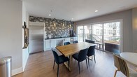 Located at 5555 E Mockingbird Lane in Dallas, TX, this single-floor community amenity space is thoughtfully designed to encourage socializing, entertainment, and productivity. The open floor plan seamlessly connects multiple functional zones, all unified by warm wood-tone flooring and a contemporary, upscale aesthetic.

The main lounge area is anchored by a plush, deep-blue sectional sofa and accented with decorative gold circular wall art and a wall-mounted flat-screen TV. Large sliding glass doors flood the space with natural light and provide direct access to an outdoor balcony overlooking the surrounding community. Adjacent to the lounge is a dedicated game area featuring a full-length shuffleboard table, a pool table, and additional seating along a navy blue bench with decorative throw pillows — all set against a striking gold geometric wall installation.

The kitchen and dining area offers a functional catering setup with white cabinetry, dark countertops, a large stainless steel refrigerator, and an eye-catching patterned mosaic tile accent wall. A solid wood communal dining table with seating for six anchors the space, with sliding doors opening to the balcony beyond.

A private meeting room provides a more intimate setting, furnished with a sleek marble-top round table, modern white chairs, a wall-mounted TV, and a bold abstract art piece beneath a sculptural gold chandelier — ideal for small gatherings or focused work sessions.