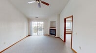 This single-floor residence offers a well-organized layout designed for comfortable everyday living. The spacious living room serves as the centerpiece of the home, showcasing dramatic vaulted ceilings, plush wall-to-wall carpeting, and a ceiling fan that enhances airflow throughout. A corner gas fireplace with a built-in niche above adds both warmth and character, while sliding glass doors flood the room with natural light and provide direct access to an outdoor balcony or patio. The adjacent dining area connects seamlessly to the kitchen via a convenient pass-through window, complemented by a decorative pendant light fixture. The kitchen is well-appointed with warm oak cabinetry, white appliances including a refrigerator, electric range, built-in microwave, and dishwasher, along with light tile flooring and ample counter space. The bedrooms are generously sized, each featuring soft carpeting, neutral walls, and windows that bring in natural views of surrounding greenery. One bedroom includes a closet with oak doors for added storage. Two full bathrooms serve the home, each finished with oak vanities, light tile flooring, large mirrors, and vanity lighting, providing a clean and functional design throughout.