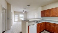 Located at 15059 Caseta Dr in Houston, TX, this single-floor residence offers a well-organized layout with 2 bedrooms, 2 bathrooms, a kitchen, living room, laundry area, and three closets. The kitchen is a standout feature, equipped with rich cherry-toned cabinetry, granite-style countertops, a full suite of white appliances including a refrigerator, range, built-in microwave, and dishwasher. A peninsula with a breakfast bar separates the kitchen from the living area, creating an open and functional flow. The living room is carpeted and brightened by a ceiling fan and a glass front door that invites natural light. Both bedrooms feature plush carpet, ceiling fans, and windows with outdoor views of greenery, providing a comfortable and airy feel. Three closets offer ample storage throughout the unit. The two bathrooms are finished with warm wood-look vinyl flooring and cherry cabinetry with granite-style countertops. The full bathroom includes a tiled tub-surround with a soaking tub, while a second bathroom provides additional vanity space. A dedicated laundry area adds everyday convenience. The neutral color palette and consistent finishes create a cohesive and practical living environment.