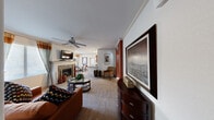 This single-floor residence offers a thoughtfully designed layout across two bedrooms and two bathrooms. The living room serves as the central gathering space, featuring crown molding, a ceiling fan, plush carpeting, and a tile-surround fireplace beneath a mounted TV—creating a cozy yet polished atmosphere. Natural light filters in through large windows dressed with layered curtains and blinds.

The dining area, finished with wood-look flooring, accommodates an intimate seating arrangement and receives natural light through a window. The galley-style kitchen is well-equipped with rich wood cabinetry, dark granite countertops, and black appliances, including a full suite of cooking and dishwashing essentials. A dedicated in-unit laundry area is conveniently accessible directly from the kitchen.

The primary bedroom connects to an en-suite bathroom through an elegant arched doorway and features soft carpeting. The second bedroom is bright and airy, with large windows allowing generous natural light. Both bathrooms are finished with wood-look flooring, warm wood vanities, and well-lit mirrors. A closet and two hallways complete the practical, efficiently organized floor plan.