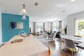 This well-appointed 2-bedroom, 2-bathroom model unit in Framingham, MA offers a thoughtfully designed single-floor layout with generous living space. The open-concept main area seamlessly connects the kitchen, dining room, and living room, creating an inviting and functional space. The modern kitchen is outfitted with light wood cabinetry, stainless steel appliances, a subway tile backsplash, and a large central island with quartz countertops and pendant lighting, ideal for both meal prep and casual dining. The dining area features a bold teal accent wall and sliding glass doors that open to a private balcony with outdoor views. The bright living room benefits from multiple windows, allowing generous natural light to fill the space. Both bedrooms are comfortably sized with plush carpeting and ample closet space, including walk-in closets with built-in shelving. The two bathrooms are finished with tile flooring, modern vanities, and glass-enclosed showers. A dedicated in-unit laundry room houses a full-size washer and dryer. Wood-style flooring flows throughout the main living areas, and four closets provide abundant storage throughout the unit.