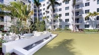 This outdoor courtyard serves as a central amenity space within a modern multi-story residential complex, blending tropical landscaping with thoughtfully designed recreational features. The space is anchored by a sleek, contemporary water feature constructed from white marble-style stone, with multiple jets creating a calm, flowing effect into a long rectangular basin. Flanking the fountain are large, bowl-shaped planters that add a sculptural element to the design.

Adjacent to the water feature is a well-maintained putting green, providing a recreational focal point within the courtyard. The artificial turf surface is neatly bordered and offers a casual space for leisure activity.

Tall, slender palm trees are strategically placed throughout the courtyard, adding vertical interest and reinforcing the tropical character of the environment. Lush, mature greenery lines the perimeter, offering a natural contrast against the crisp white exterior of the surrounding multi-story building.

The building itself features clean, modern lines with wide balconies and large windows that overlook the courtyard below, creating an open and airy atmosphere. The overall ambiance is bright, resort-inspired, and inviting, reflecting a lifestyle-oriented approach to communal outdoor living.