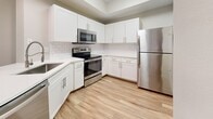 This 1,050-square-foot single-floor residence at 10135 Gate Parkway North in Jacksonville, FL offers 2 bedrooms and 3 bathrooms across a well-designed, functional layout. Wood-look flooring runs throughout the entire unit, providing a cohesive and low-maintenance aesthetic. The open-concept kitchen and living area serves as the heart of the home, featuring white shaker cabinetry, subway tile backsplash, stainless steel appliances including a refrigerator, range, and microwave, and a peninsula with a sink that flows seamlessly into the living space. The primary bedroom spans 170 square feet, is highlighted by crown molding, dual windows with blinds, and a ceiling fan. Its en-suite bathroom includes a dual-sink vanity with gray cabinetry, a large mirror, and a walk-in shower with subway tile surround and a sliding glass door. A walk-in closet with wire shelving provides ample storage. The secondary bedroom features a ceiling fan, a closet door, and a bright window with outdoor views. Secondary bathrooms include a tub/shower combo with clean white tile surrounds. Natural light flows through multiple windows across the unit, and a glass exterior door offers additional outdoor access.