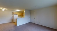 Located at 1614 C Ashby, this single-floor unit offers a practical and well-organized layout designed for everyday living. The open-concept design connects the kitchen and living area seamlessly, creating a sense of spaciousness throughout. The kitchen is equipped with warm honey-toned wood cabinetry, a white refrigerator, and a built-in microwave, with countertops that extend into a peninsula-style breakfast bar — ideal for casual dining or meal prep. The kitchen benefits from overhead flush-mount lighting that keeps the space bright and functional. The living area is finished with plush carpeting in a neutral tone, providing a comfortable and cohesive feel. A paneled entry door with a standard lock is visible, offering straightforward access to the unit. The neutral wall tones throughout create a clean, move-in-ready aesthetic that allows for easy personalization. The overall layout is efficient and thoughtfully arranged, making good use of the available floor space while maintaining an open, airy atmosphere. This unit is well-suited for those seeking a straightforward, single-level living arrangement with key amenities conveniently accessible.
