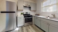 This single-floor residence offers a well-organized layout with a cohesive, contemporary aesthetic carried throughout each room. The flooring is a standout feature, with gray-toned hardwood-style planks running consistently across the living areas and bedrooms, lending a modern and unified feel to the entire space.

The kitchen has been thoughtfully updated with gray shaker-style cabinetry, white quartz-look countertops, and a classic white subway tile backsplash. Stainless steel appliances, including a gas range and full-size refrigerator, provide a functional and polished finish. A window above the counter allows natural light to brighten the workspace.

The living and bedroom areas are bright and open, with crisp white walls and natural light filtering through slatted blinds on multiple windows. One bedroom benefits from dual windows, enhancing ventilation and light, while another features a single window and convenient door access. A hallway closet provides additional built-in storage.

The bathroom is clean and well-appointed, featuring a full soaking tub with a tiled surround, a window for natural ventilation, and matching hardwood-style flooring. The overall ambiance of the space is fresh, neutral, and move-in ready, making it a practical and inviting home.
