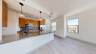 Located at 8150 Rafael Rivera Way in Las Vegas, NV, this well-appointed residence offers five bedrooms and three bathrooms across a single floor. The open-concept kitchen and living area serves as the heart of the home, showcasing warm wood cabinetry, sleek gray countertops, a large kitchen island with pendant lighting, and a full suite of stainless steel appliances including a gas range, microwave, and French door refrigerator. Large windows in the living area flood the space with natural light and offer views of the surrounding Las Vegas community. The bedrooms are bright and generously sized, with light wood-style flooring or plush carpet, and windows that bring in ample daylight. The primary bedroom includes dedicated closet space with built-in shelving and hanging rods for organized storage. The bathrooms are finished with wood-toned vanities, gray countertops, and clean white subway tile surrounding the tub-shower combinations. Wide hallways with tray ceiling details connect the rooms with an airy, modern feel. A dedicated in-unit laundry room with shelving and side-by-side washer and dryer adds everyday convenience. Crisp white walls and consistent light-toned flooring throughout give the entire residence a cohesive, contemporary aesthetic.