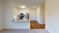 Located at 2004 Calvary Circle in Charlottesville, Virginia, this single-floor unit offers a well-designed layout that balances functionality with comfortable living. The open-concept kitchen serves as a central hub, featuring white shaker-style cabinetry, granite countertops, and a full suite of stainless steel appliances including a refrigerator, electric range with microwave above, and a sink integrated into the peninsula. The peninsula itself provides a natural divider between the kitchen and the living area, making the space ideal for both everyday use and entertaining.

Hardwood-style flooring runs through the kitchen and entryway, while plush carpeting extends throughout the living room and bedrooms, adding warmth and comfort. The living area benefits from multiple windows fitted with horizontal blinds, allowing ample natural light to fill the space. Crown molding accents the living room, adding a subtle architectural detail.

The bedroom is generously sized with corner windows on two walls, maximizing natural light and views of the surrounding greenery. A walk-in closet provides practical storage. The bathroom features a full tub-shower combination with white and neutral tile accents and hardwood-style flooring. The unit also includes a dedicated utility/laundry area with additional cabinetry and granite countertop space.