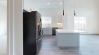 This contemporary two-floor space makes a striking first impression with its soaring double-height living area, flooded with natural light through an abundance of large windows that frame sweeping city skyline and mountain views. A sleek black spiral staircase serves as a sculptural centerpiece, connecting the two levels with an industrial-modern flair, complemented by clean white walls and durable wood-look flooring throughout the main living area.

The open-concept kitchen is thoughtfully designed with crisp white upper cabinetry, gray lower cabinetry, white quartz countertops, and a classic subway tile backsplash. Stainless steel appliances, including a refrigerator, range, over-the-range microwave, and dishwasher, lend a polished look. A central island with elegant pendant lighting overhead adds both function and style to the space.

Bedrooms feature plush carpeting and well-sized windows that bring in natural light and scenic views. The bathroom is finished with large-format tile flooring, a gray vanity with brass hardware, and a tiled shower-tub combination. Generous walk-in closet space provides ample storage. The upper floor, accessible via the spiral staircase, extends the living options with an open loft-style layout. Throughout, the design palette of whites, grays, and black accents creates a cohesive, modern aesthetic.