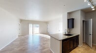 This single-story home showcases a thoughtfully designed open-concept layout that seamlessly connects the kitchen, dining, and living areas. Light-toned wood-look flooring extends throughout the space, complementing the neutral palette of warm beige and white walls that enhance the sense of openness and brightness.

The kitchen is well-appointed with dark espresso cabinetry, granite countertops, a double-basin undermount sink, and black appliances, including a range, microwave, and refrigerator. A peninsula with additional cabinetry provides both workspace and a natural visual boundary between the kitchen and living area. The living space is generously proportioned and benefits from abundant natural light streaming through a sliding glass door that opens to the exterior.

Bedrooms are served by elegant orb-style pendant chandeliers and receive ample natural light through well-placed windows. The primary bedroom connects to a private en suite bathroom featuring a granite-topped dark vanity and a spacious walk-in closet with wire shelving. A second full bathroom mirrors the same design aesthetic, while a compact half bath with a pedestal sink serves as a convenient powder room. A dedicated laundry room includes a full-size washer and dryer with overhead cabinetry for storage.