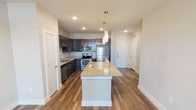 Located at 751 N Main St in Mansfield, Texas, this single-floor residence offers a thoughtfully designed open-concept layout with contemporary finishes throughout. The kitchen serves as a central highlight, showcasing dark espresso cabinetry, granite countertops, a large central island with pendant lighting overhead, and a full suite of stainless steel appliances including a refrigerator, range, microwave, and dishwasher. Wood-look plank flooring runs throughout the main living areas, complementing the clean, neutral color palette and recessed lighting above.

The living area is generously proportioned, featuring a ceiling fan, track lighting, and French doors with transom windows that invite natural light and provide outdoor access. The bedroom spaces are carpeted for comfort, with neutral tones, ceiling fans, and windows fitted with blinds allowing for controlled natural light.

The bathroom is well-appointed with wood-look flooring, a granite-topped dark vanity with an undermount sink, a full soaking tub and shower combination with large-format tile surround, and a framed mirror. The overall ambiance of the space is modern and clean, offering a functional and comfortable living environment in the heart of Mansfield, TX.