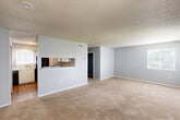 This two-story home in Baton Rouge, Louisiana offers a functional and straightforward layout spread across two floors. The main level houses a combined kitchen and living area, where the kitchen features white cabinetry, laminate countertops, hardwood-style flooring, and black appliances including a range, dishwasher, and refrigerator. A pass-through window connects the kitchen to the living area, which is finished with neutral carpet and benefits from natural light through a side window. The upper floor is dedicated entirely to the four bedrooms, accessible via a central staircase and connected by hallways. The spacious primary bedroom stands out with two windows that invite generous natural light and views of the surrounding greenery, complemented by a ceiling fan. The additional bedrooms are similarly carpeted, each featuring ceiling fans and windows with blinds. Two closets provide storage solutions throughout the upper level. The full bathroom includes a vanity with a speckled countertop and a separate tub/shower room with hardwood-style flooring. Textured ceilings are consistent throughout the home, and the neutral gray and white color palette creates a clean, cohesive aesthetic across all rooms.