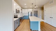 Located at 13972 Edgewood Ave in Savage, MN, this thoughtfully designed one-bedroom, one-bathroom unit offers a modern and functional layout across a single floor. The open-concept living and kitchen area serves as the heart of the space, showcasing a striking kitchen with two-tone cabinetry — white upper cabinets paired with soft blue-gray lower cabinets — complemented by a white quartz center island, stainless steel appliances, a tile backsplash, and stylish geometric pendant lighting. Light hardwood-style flooring flows throughout the main living areas, enhancing the bright, airy ambiance. The living area features a sliding glass door that opens to a private balcony, offering pleasant outdoor views and abundant natural light. The bedroom is a comfortable retreat with plush carpeting, a large window framing greenery views, and a dedicated closet with built-in shelving. The bathroom is finished with clean, contemporary details including a white shaker-style vanity, white quartz countertop, a bold black-framed mirror, and matching matte black hardware and fixtures. Additional storage is provided via a dedicated closet. The overall aesthetic is clean, modern, and move-in ready.