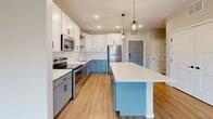Located at 13972 Edgewood Ave in Savage, MN, this thoughtfully designed one-bedroom, one-bathroom unit offers a modern and functional layout across a single floor. The open-concept living and kitchen area serves as the heart of the space, showcasing a striking kitchen with two-tone cabinetry — white upper cabinets paired with soft blue-gray lower cabinets — complemented by a white quartz center island, stainless steel appliances, a tile backsplash, and stylish geometric pendant lighting. Light hardwood-style flooring flows throughout the main living areas, enhancing the bright, airy ambiance. The living area features a sliding glass door that opens to a private balcony, offering pleasant outdoor views and abundant natural light. The bedroom is a comfortable retreat with plush carpeting, a large window framing greenery views, and a dedicated closet with built-in shelving. The bathroom is finished with clean, contemporary details including a white shaker-style vanity, white quartz countertop, a bold black-framed mirror, and matching matte black hardware and fixtures. Additional storage is provided via a dedicated closet. The overall aesthetic is clean, modern, and move-in ready.