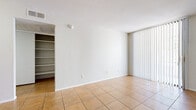 This single-floor residence offers a clean, functional layout designed for comfortable everyday living. The main living and dining areas are finished with warm-toned ceramic tile flooring and feature large sliding glass doors dressed with vertical blinds, allowing generous natural light to fill the space. A built-in shelving unit in the living area provides convenient storage and display options. The open-concept design connects the living and dining zones seamlessly, with the dining area accented by a classic chandelier overhead. The galley-style kitchen is well-equipped with warm wood cabinetry, ample counter space, a double sink, and white appliances including a refrigerator, dishwasher, electric range, and microwave. A pass-through counter connects the kitchen to the dining area, enhancing the open feel. The bedroom is carpeted for comfort, features a ceiling fan, and enjoys direct outdoor access through a sliding glass door, bringing in natural light and fresh air. The bathroom is generously appointed with an extended wood-toned vanity, dual mirrors, bright overhead lighting, a full soaking tub, and tile flooring. Throughout the space, neutral white walls and consistent finishes create a bright, cohesive ambiance well-suited for a variety of furnishing styles.
