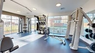 Located at 22 Georgetown Road in New London, Connecticut, this fitness center offers a comprehensive workout environment designed to accommodate a wide range of exercise needs. The space is thoughtfully laid out across a single floor, providing ample room for both cardio and strength training activities.

Large floor-to-ceiling windows line one wall of the facility, flooding the interior with natural light and offering views of the surrounding landscape, creating an open and energizing atmosphere. The cardio zone features multiple treadmills, an elliptical trainer, and a stationary bike, all positioned to take advantage of the expansive window views.

The strength training area is equally well-appointed, housing a multi-function cable machine, a dedicated training zone rack with TRX suspension straps, medicine balls, and stability balls. A full dumbbell rack with a comprehensive range of free weights is positioned against a wall-length mirror, which visually expands the space and aids in maintaining proper form during workouts.

Adjustable weight benches are distributed throughout for versatile use across multiple exercise stations. The flooring transitions between cushioned rubber tiles in the equipment zones and a smooth, durable surface in the open training areas. Recessed flush-mount ceiling lights provide consistent, even illumination throughout. The crisp white walls and clean design aesthetic contribute to a bright, modern, and motivating fitness environment.