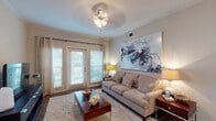 This single-floor residence offers a thoughtfully designed layout with distinct living, dining, kitchen, bedroom, and bathroom areas that work together to create a cohesive and comfortable living environment. The living room serves as the central gathering space, featuring crown molding, wood-look flooring, a ceiling fan with light fixture, and a set of French doors that invite natural light and provide outdoor access. A large statement painting anchors one wall, lending the room a contemporary character. The adjoining dining area is defined by wainscoting along the lower walls, warm hardwood-style flooring, and an elegant chandelier overhead that sets a refined atmosphere for meals. The kitchen is outfitted with dark espresso cabinetry, granite-style countertops, and matching black appliances, including a range, built-in microwave, and refrigerator, creating a bold and functional cooking space. The bedroom is a serene retreat, carpeted for comfort, with a ceiling fan, generous natural light from a large window, and a walk-in closet providing ample storage. The bathroom includes a soaking tub and shower combination with a curved curtain rod, a dark vanity, and wood-look flooring, completing the space with practical elegance throughout.