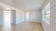 Located at 12401 North 15th Street in Tampa, Florida, this single-story, 2-bedroom, 1-bathroom residence offers a straightforward and functional layout. Throughout the home, large-format beige tile flooring provides a cohesive look, complemented by white baseboards and textured ceilings.

The living area is bright and open, featuring a distinctive white grid-pattern accent wall that adds a subtle visual element to the space. A sliding glass door fills the room with natural light and provides direct outdoor access. The living area flows seamlessly into the kitchen, which is equipped with warm-toned wood cabinetry, a white refrigerator, and a white range, offering practical functionality.

Both bedrooms continue the tile flooring and share the grid-pattern wall detailing. The primary bedroom is a comfortable size and includes a sliding-door closet with built-in hanging storage. Windows fitted with blinds allow for natural light while maintaining privacy. The second bedroom also features a window with an exterior view.

The full bathroom is finished in an all-white palette, featuring a tub-shower combination, a toilet, and a single vanity with a mirror, maintaining a clean and utilitarian aesthetic throughout. A dedicated closet provides additional storage. The home's consistent design elements create a cohesive and easy-to-maintain living environment.