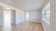Located at 12401 North 15th Street in Tampa, Florida, this single-story, 2-bedroom, 1-bathroom residence offers a straightforward and functional layout. Throughout the home, large-format beige tile flooring provides a cohesive look, complemented by white baseboards and textured ceilings.

The living area is bright and open, featuring a distinctive white grid-pattern accent wall that adds a subtle visual element to the space. A sliding glass door fills the room with natural light and provides direct outdoor access. The living area flows seamlessly into the kitchen, which is equipped with warm-toned wood cabinetry, a white refrigerator, and a white range, offering practical functionality.

Both bedrooms continue the tile flooring and share the grid-pattern wall detailing. The primary bedroom is a comfortable size and includes a sliding-door closet with built-in hanging storage. Windows fitted with blinds allow for natural light while maintaining privacy. The second bedroom also features a window with an exterior view.

The full bathroom is finished in an all-white palette, featuring a tub-shower combination, a toilet, and a single vanity with a mirror, maintaining a clean and utilitarian aesthetic throughout. A dedicated closet provides additional storage. The home's consistent design elements create a cohesive and easy-to-maintain living environment.