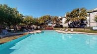 Located at 1708 Timberline Dr in Benbrook, Texas, this single-story community amenity space is part of the Siena residential community. The property centers around a generously sized outdoor swimming pool with clear turquoise water, surrounded by a spacious concrete pool deck lined with lounge chairs — ideal for relaxing under the Texas sun. Mature trees border the area, providing natural shade and a sense of privacy, while black iron fencing encloses the grounds for added security.

A covered patio area serves as a comfortable outdoor lounge, distinguished by its craftsman-inspired architecture featuring arched stucco columns, ceiling fans, and a gated iron entry. The interior of this covered space is finished with clean white shiplap walls, crown molding, and recessed lighting, creating a polished yet relaxed atmosphere. Cushioned seating and a coffee table arranged on a woven area rug offer a welcoming spot for gathering. An open side of the patio frames views of the pool deck and surrounding greenery, seamlessly connecting the indoor and outdoor environments. A small refrigeration unit nearby adds a practical touch to the lounge. The overall ambiance is inviting, well-maintained, and thoughtfully designed for community enjoyment.