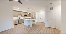 This thoughtfully designed 950-square-foot apartment offers 2 bedrooms and 2 bathrooms across a single floor, delivering a clean, modern aesthetic throughout. The open-concept kitchen and living area serves as the heart of the home, anchored by a large white-quartz island with built-in shelving. The kitchen features light wood-grain cabinetry, a white tile backsplash, stainless steel appliances including a refrigerator, range, microwave, and dishwasher, all illuminated by recessed lighting and globe pendant fixtures. Light wood-look flooring runs seamlessly throughout the entire unit. The primary bedroom, measuring 140 square feet, includes a ceiling fan, a large window for natural light, and direct access to a private balcony with exterior views. It is complemented by a spacious walk-in closet featuring multi-tiered wood hanging rods and shelving. The en-suite primary bathroom boasts a dual-sink blue vanity with white quartz countertops, a lighted mirror, and a tiled walk-in shower with a glass door. The second bedroom also features a ceiling fan and a bright window. The second bathroom mirrors the same refined design, with a blue vanity, lighted mirror, and a tiled tub-shower combination with matte black fixtures. A second closet provides additional storage throughout the unit.
