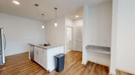 This thoughtfully designed one-bedroom, one-bathroom residence offers a compact yet functional layout across a single floor. The open-concept kitchen serves as the heart of the space, featuring granite countertops, white shaker cabinetry, a subway tile backsplash, and a full suite of stainless steel appliances including a gas range, over-the-range microwave, and side-by-side refrigerator with ice and water dispenser. A peninsula with pendant lighting provides additional counter space and a casual dining area, complemented by a built-in granite shelf on the adjacent wall. Warm wood-look flooring flows seamlessly throughout the main living areas and bedroom, creating a cohesive and inviting atmosphere. The bedroom is a comfortable, well-proportioned retreat featuring a ceiling fan, a window with natural light and exterior views, and a built-in shelving unit for added storage. The bathroom is finished with light tile flooring, a granite-topped vanity, a full soaking tub with shower, and a large double-door closet providing generous storage. Clean white walls and a bright, neutral palette throughout give the space a fresh, modern feel.