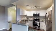 This single-floor residence offers a thoughtfully designed layout centered around a standout kitchen that blends style and functionality. The kitchen features crisp white cabinetry with brushed nickel hardware, providing ample storage and a clean, bright aesthetic. Granite countertops in a cool blue-grey tone add a touch of elegance, while a peninsula-style counter extends the workspace and creates a natural division between the kitchen and adjoining living areas. Stainless steel appliances, including a gas range, built-in microwave, and a double-basin sink, equip the space for everyday culinary use. Track lighting mounted to the ceiling ensures the workspace is well-lit and functional. Hardwood-style flooring runs throughout, lending warmth and continuity to the space. A textured ceiling and neutral wall tones contribute to a relaxed, inviting ambiance. The open sightlines between the kitchen and adjacent spaces enhance the overall sense of flow, making this residence practical for both daily living and casual entertaining.