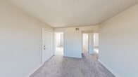 Located at 4 Suburban Cir in Portsmouth, Virginia, this single-floor residence offers a straightforward and functional layout designed for comfortable everyday living. The interior is finished with neutral tones throughout, creating a clean and bright atmosphere across all rooms.

The living areas feature wall-to-wall carpeting in a soft gray hue, lending warmth and continuity to the space. Multiple rooms benefit from generously sized windows fitted with horizontal blinds, allowing abundant natural light to filter in while offering views of the surrounding neighborhood. The open, uncluttered design of each room provides a versatile canvas for a variety of furniture arrangements.

The kitchen is a practical and well-equipped space, featuring warm wood-toned cabinetry, light countertops, a double sink, a coil-top range, and a full-size refrigerator. Light-toned vinyl plank flooring adds a clean, durable finish, and a window above the sink area brings in additional natural light.

A bathroom with wood-toned vanity cabinetry and hard surface flooring connects conveniently to the adjoining carpeted spaces. Throughout the home, white panel doors, clean baseboards, and a consistent neutral color palette contribute to a cohesive and well-maintained interior. The overall layout, as seen in the dollhouse view, reflects a compact yet efficiently organized floor plan.