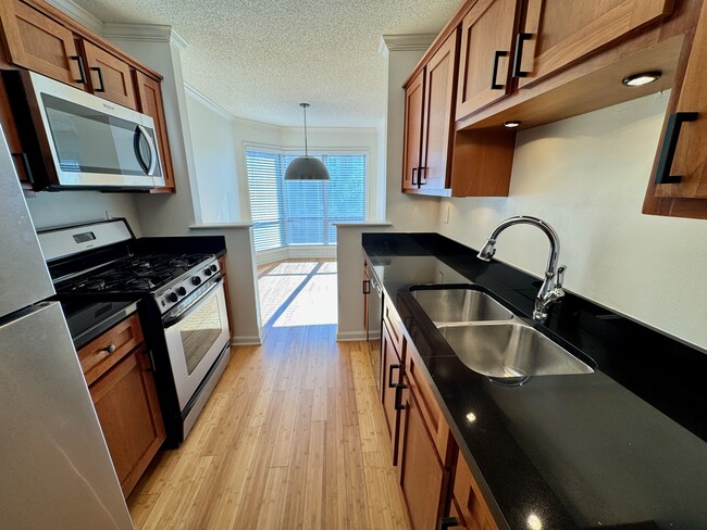 kitchen with cherry cabinets, granite counters, stainless/black appliances, dining room at end - 209 14th St. NE #119