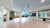 Located at 115 Healthy Way in Folsom, CA, this single-floor fit and wellness studio is thoughtfully designed to support a full range of fitness and wellness activities. The space is divided into distinct functional zones, each finished with care and attention to detail.

The open wellness studio is a bright, airy space featuring light hardwood flooring, a soft blue tray ceiling with decorative crown molding, and multiple ceiling fans that promote comfortable airflow. Large windows and French doors flood the room with natural light and provide views of the outdoor surroundings. A large wall-mounted flat-screen display and framed mirror panels add both functionality and visual depth, while TRX suspension trainers mounted along one wall support versatile strength training.

The fitness room features plush carpeted flooring and is equipped with treadmills, ellipticals, a rowing machine, multi-station strength equipment, and benches. Full-length wall mirrors amplify the sense of space and allow users to monitor their form. Coffered ceilings and recessed lighting create an energetic yet polished atmosphere.

The entrance area sets an inviting tone with light hardwood floors, a soft blue ceiling, large vintage athletic-themed artwork, a frosted glass sliding partition, and ceiling fans, transitioning seamlessly into the studio beyond.