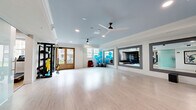 Located at 115 Healthy Way in Folsom, CA, this single-floor fit and wellness studio is thoughtfully designed to support a full range of fitness and wellness activities. The space is divided into distinct functional zones, each finished with care and attention to detail.

The open wellness studio is a bright, airy space featuring light hardwood flooring, a soft blue tray ceiling with decorative crown molding, and multiple ceiling fans that promote comfortable airflow. Large windows and French doors flood the room with natural light and provide views of the outdoor surroundings. A large wall-mounted flat-screen display and framed mirror panels add both functionality and visual depth, while TRX suspension trainers mounted along one wall support versatile strength training.

The fitness room features plush carpeted flooring and is equipped with treadmills, ellipticals, a rowing machine, multi-station strength equipment, and benches. Full-length wall mirrors amplify the sense of space and allow users to monitor their form. Coffered ceilings and recessed lighting create an energetic yet polished atmosphere.

The entrance area sets an inviting tone with light hardwood floors, a soft blue ceiling, large vintage athletic-themed artwork, a frosted glass sliding partition, and ceiling fans, transitioning seamlessly into the studio beyond.