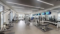 The IMT Sonoma Hills fitness center is a thoughtfully designed, single-floor facility that provides a comprehensive workout environment. The space features a clean, modern aesthetic with crisp white walls, wood-look flooring, and sleek linear LED lighting that runs across the ceiling, creating a bright and energizing atmosphere. Large windows along one wall allow ample natural light to fill the cardio zone, where a row of treadmills, ellipticals, and other aerobic machines are positioned to take advantage of the outdoor views.

The strength training area is well-appointed with cable machines, free weight racks, adjustable benches, and multi-functional weight stations, catering to a wide range of workout styles and fitness levels. Floor-to-ceiling mirrors along one wall visually expand the space while allowing users to monitor their form. Multiple flat-screen televisions are mounted throughout, offering entertainment during workouts.

A dedicated functional training zone includes stability balls, medicine balls, resistance bands, and exercise mats, providing space for stretching and dynamic movement. Contemporary artwork decorates the walls near the entrance, adding a polished, welcoming touch. Access is provided through bold black-framed glass double doors, reinforcing the facility's modern design sensibility throughout.