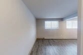 Located on Jamesville Avenue in Syracuse, NY, this one-bedroom, one-bathroom unit offers a practical and efficiently organized single-floor layout. The living room is the largest area of the unit, featuring durable grey wood-style plank flooring, neutral light grey walls, and two windows fitted with horizontal blinds that allow natural light to fill the space. A baseboard heating system runs along the exterior walls throughout the unit, ensuring consistent warmth. The bedroom is a cozy, private space with its own window and baseboard heater, maintaining the same flooring and clean aesthetic found throughout. The kitchen is equipped with white cabinetry offering ample upper and lower storage, light speckled countertops, a stainless steel sink, and under-cabinet lighting. The bathroom includes a full tub and shower combination with a curtain rod and brushed nickel fixtures. A dedicated vanity area with a lighted mirror and built-in shelf is conveniently located adjacent to two closets, providing functional storage solutions. The entrance leads smoothly into the main living area, giving the unit a logical and accessible flow. Overall, the space presents a clean, move-in ready environment with consistent finishes throughout.