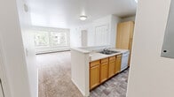 Located at 7545 Foxridge Way in Anchorage, Alaska, this two-bedroom, two-bathroom residence offers a functional single-floor layout designed for comfortable everyday living. The open-concept kitchen flows directly into the living room, creating a connected and practical common area. The kitchen features warm honey-toned cabinetry, light countertops, a double sink set into a peninsula island, a coil-burner electric range with an over-the-range microwave, a dishwasher, and durable tile-style flooring. The living room is carpeted and filled with natural light from a large set of windows overlooking the tree-lined surroundings, while a sliding glass door provides access to an outdoor balcony. Both bedrooms are carpeted and receive natural light through window blinds, with the primary bedroom offering a comfortable, well-proportioned layout. The bathrooms are cleanly finished with light countertops and built-in storage. Throughout the residence, baseboard heating ensures warmth during Alaska's colder months. A dedicated closet adds practical storage. The bright white walls and neutral carpet tones create a clean, consistent aesthetic throughout the space.